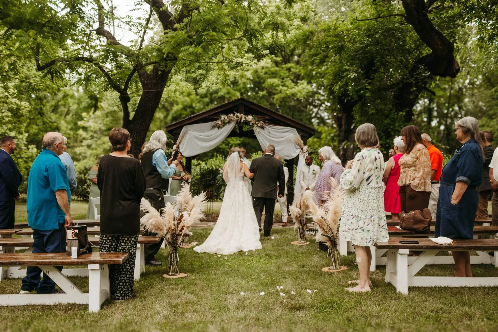 Outdoor lawn ceremony with guests seated before a draped arch at The Heritage Barn in Conover, NC