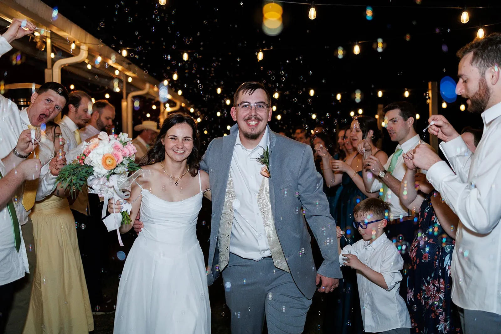 Couple celebrating with guests during a nighttime reception exit at The Heritage Barn