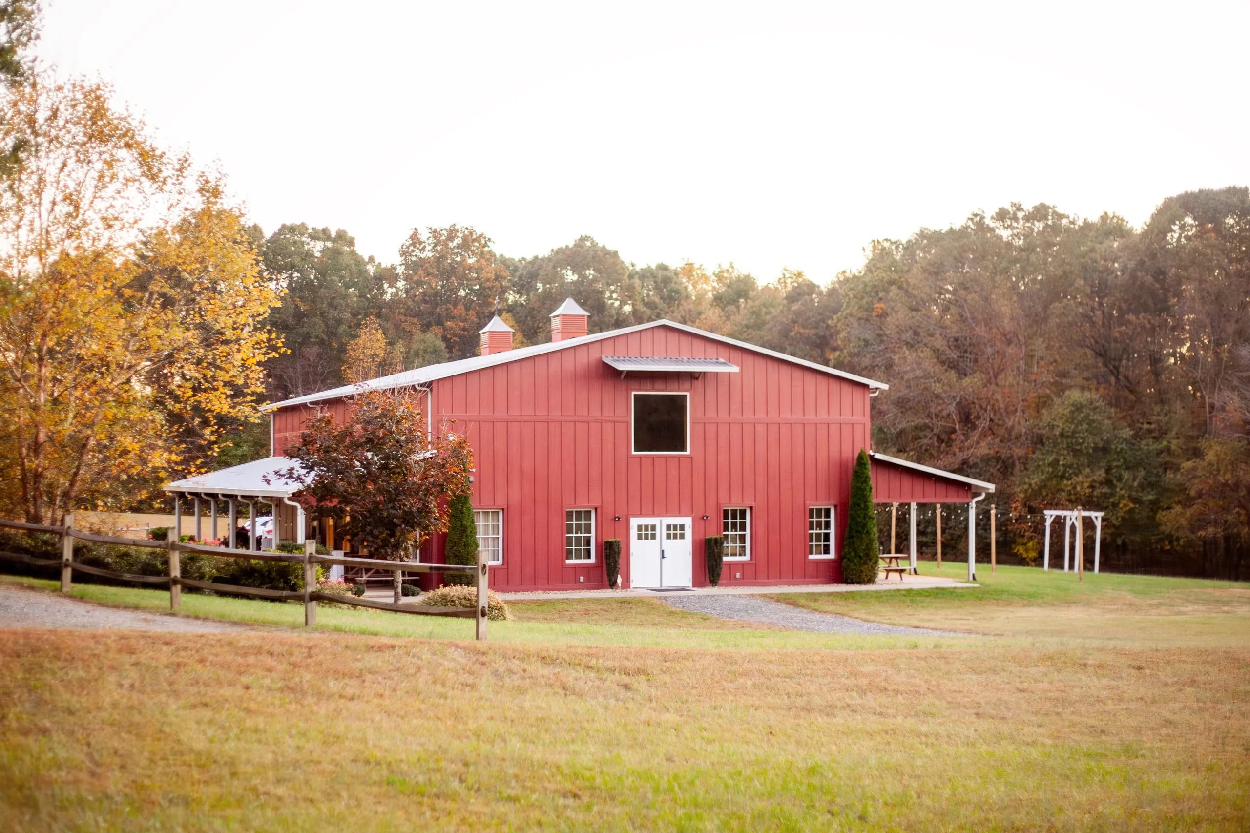 The red event barn at The Heritage Barn framed by golden autumn trees on its 30 acres in Conover, NC